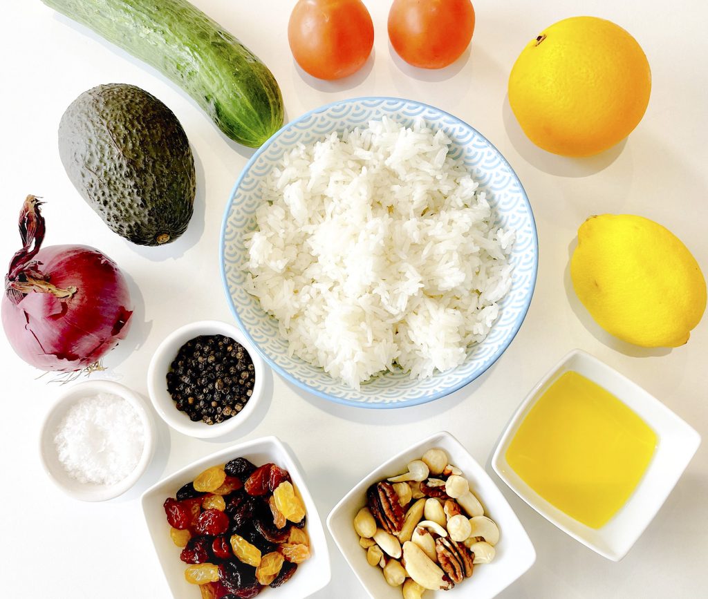 Sunlit Sovereign Rice Salad ingredients with white rice, tomato, orange, lemon, olive oil, nuts, juicy raisins, salt and pepper, red onion, avocado and cucumber in a circle.